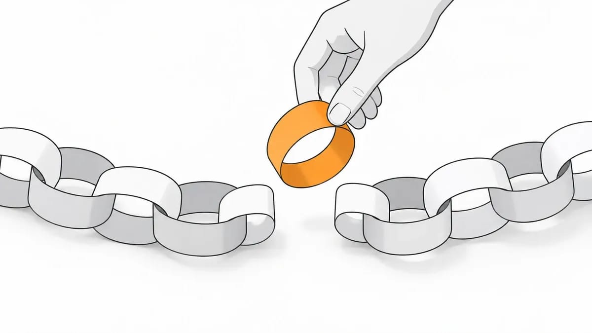 A hand holding an orange paper loop above the gap in a paper chain on a desk