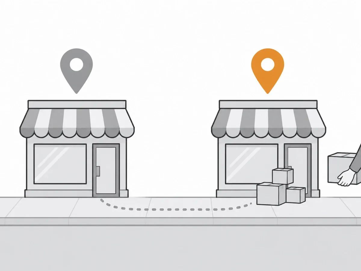 Two shopfronts on a street, the left one empty under a grey map pin and the right one with moving boxes at its door under an orange map pin, joined by a dotted path